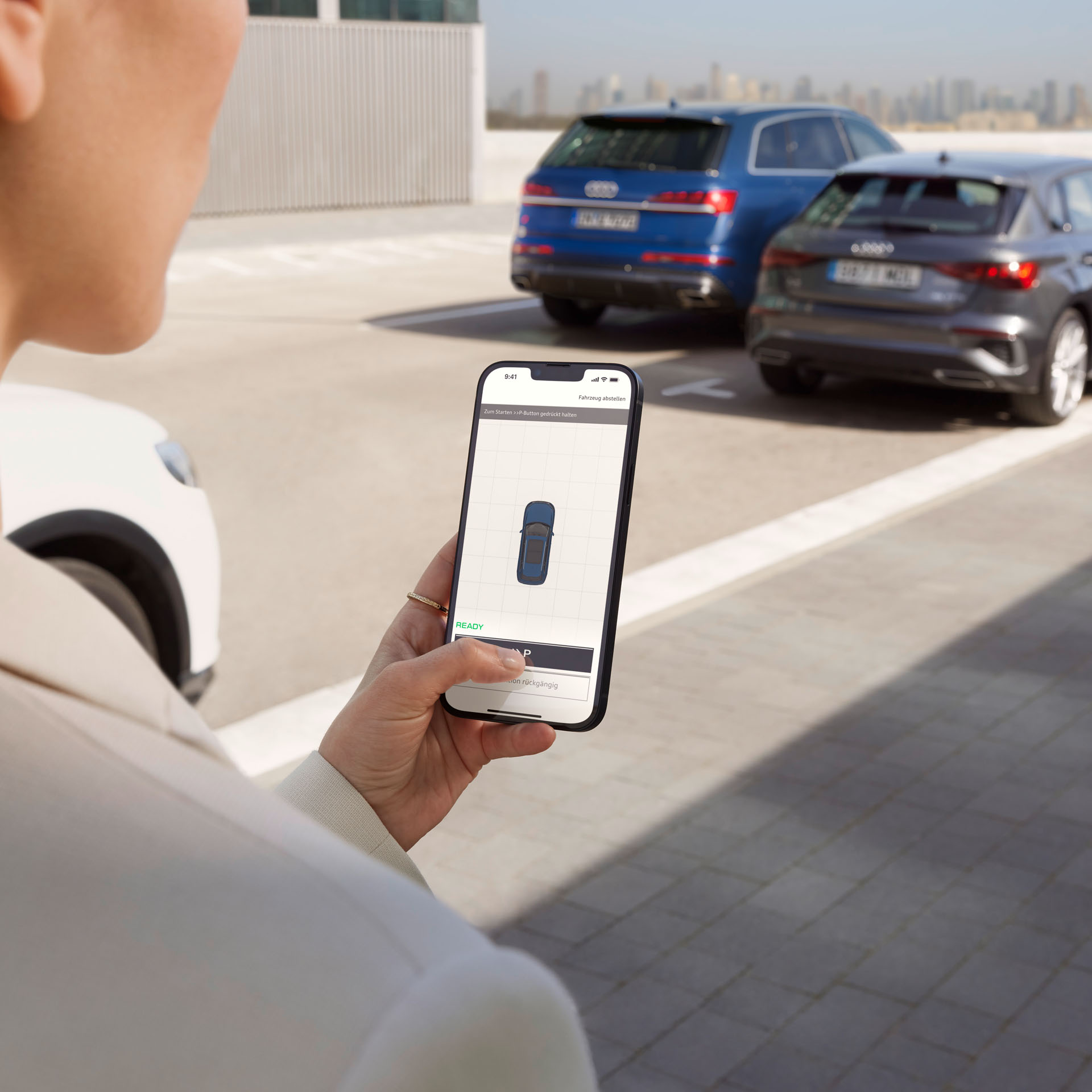 Frau hält Smartphone in der Hand und bedient den Audi Remote Parkassistenten