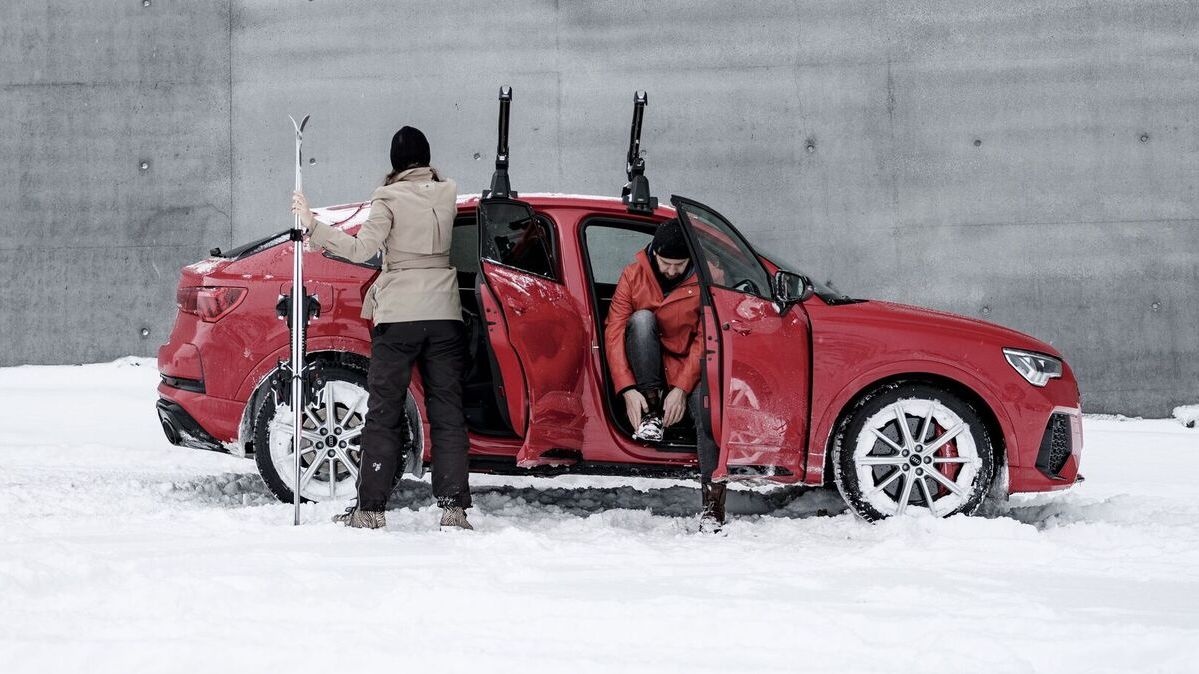 Ein Audi im Winter, eine Person sitz bei geöffneter Türe am Beifahrersitz und zieht sich Schuhe  an