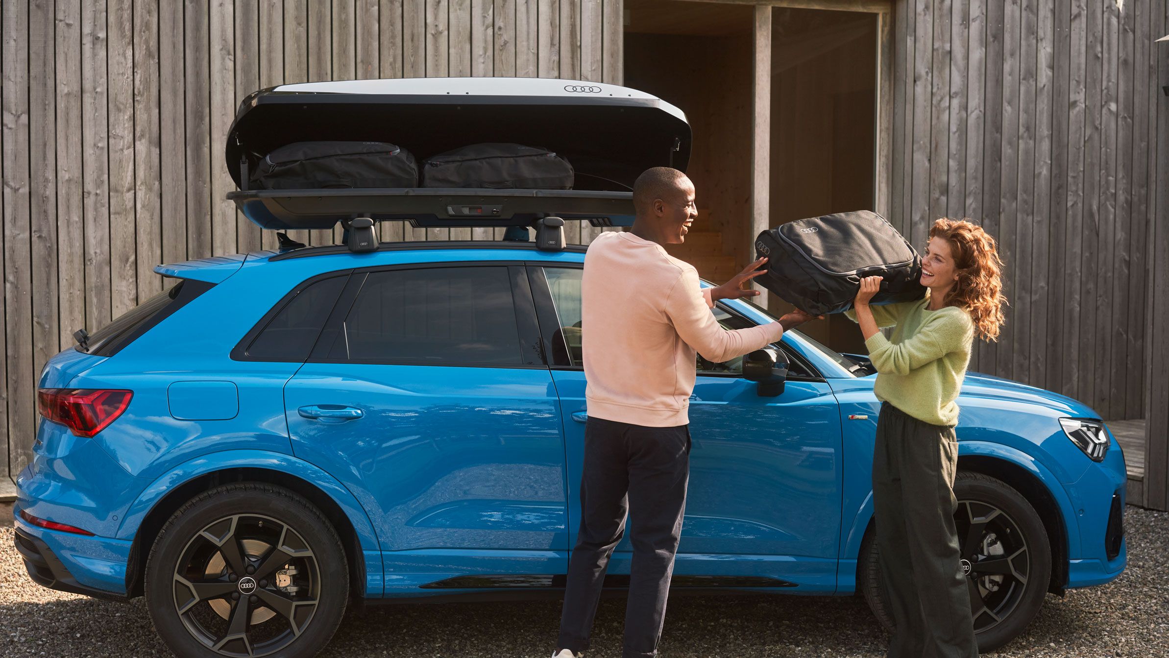 Zwei Personen beladen eine Audi Dachbox auf einem blauen Audi