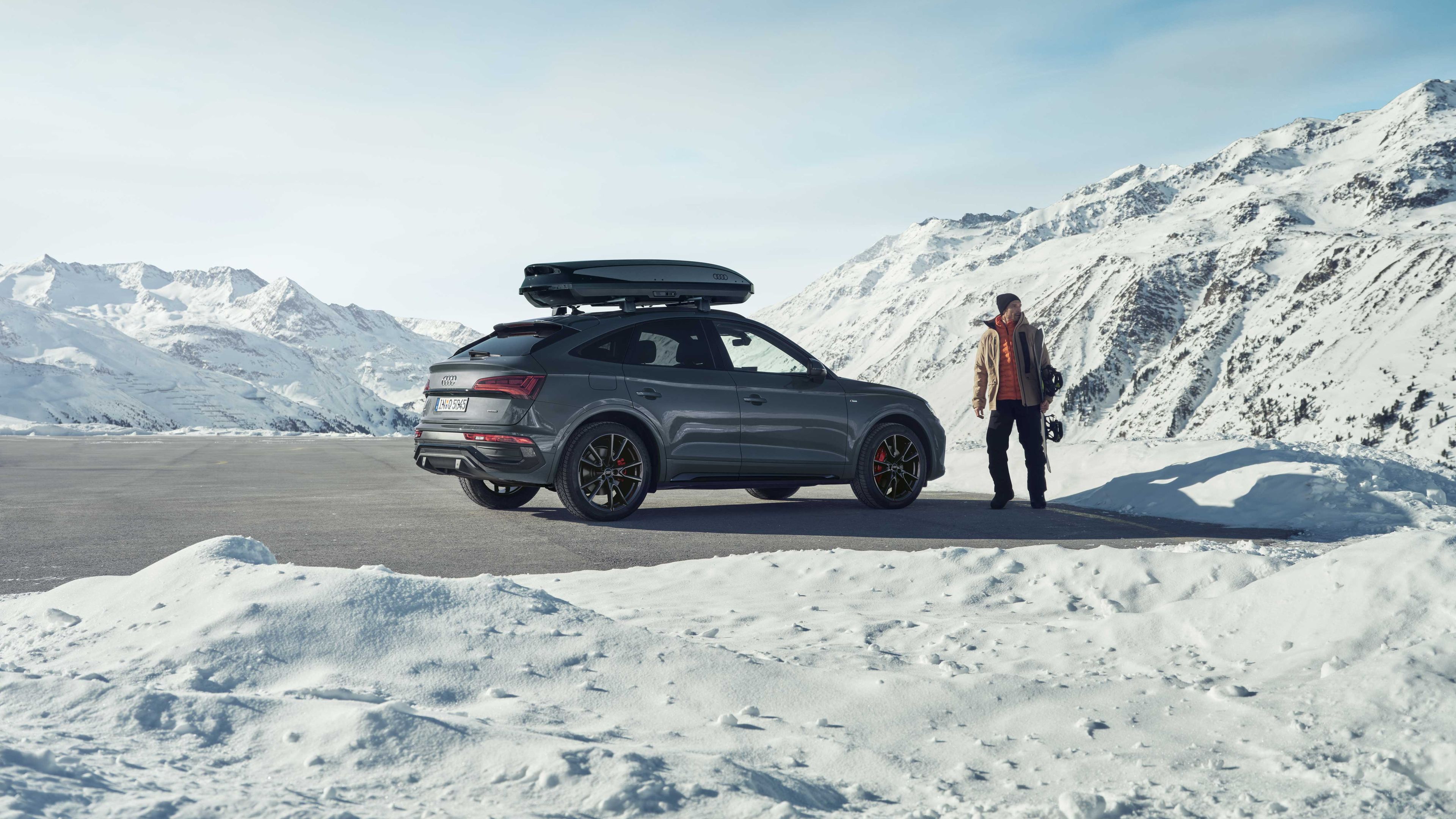 Ein Audi Q5 auf dem eine Dachbox montiert ist, parkt in winterlicher Landschaft in den Bergen