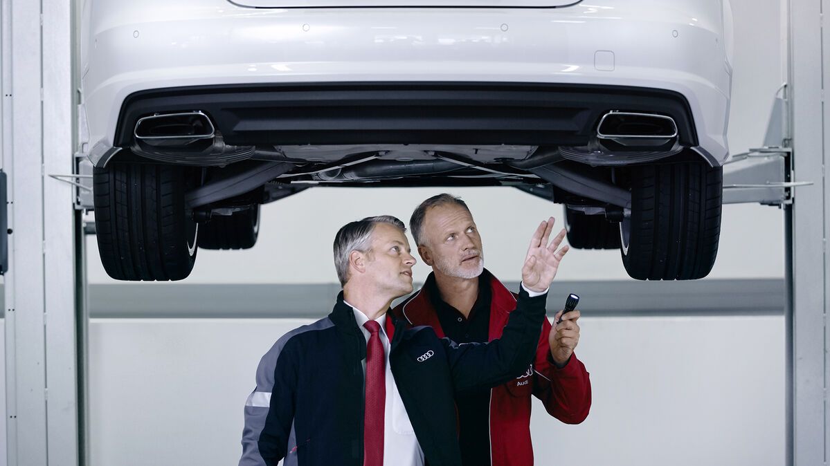Zwei Audi Techniker beraten sich zu einem Audi auf der Hebebühne