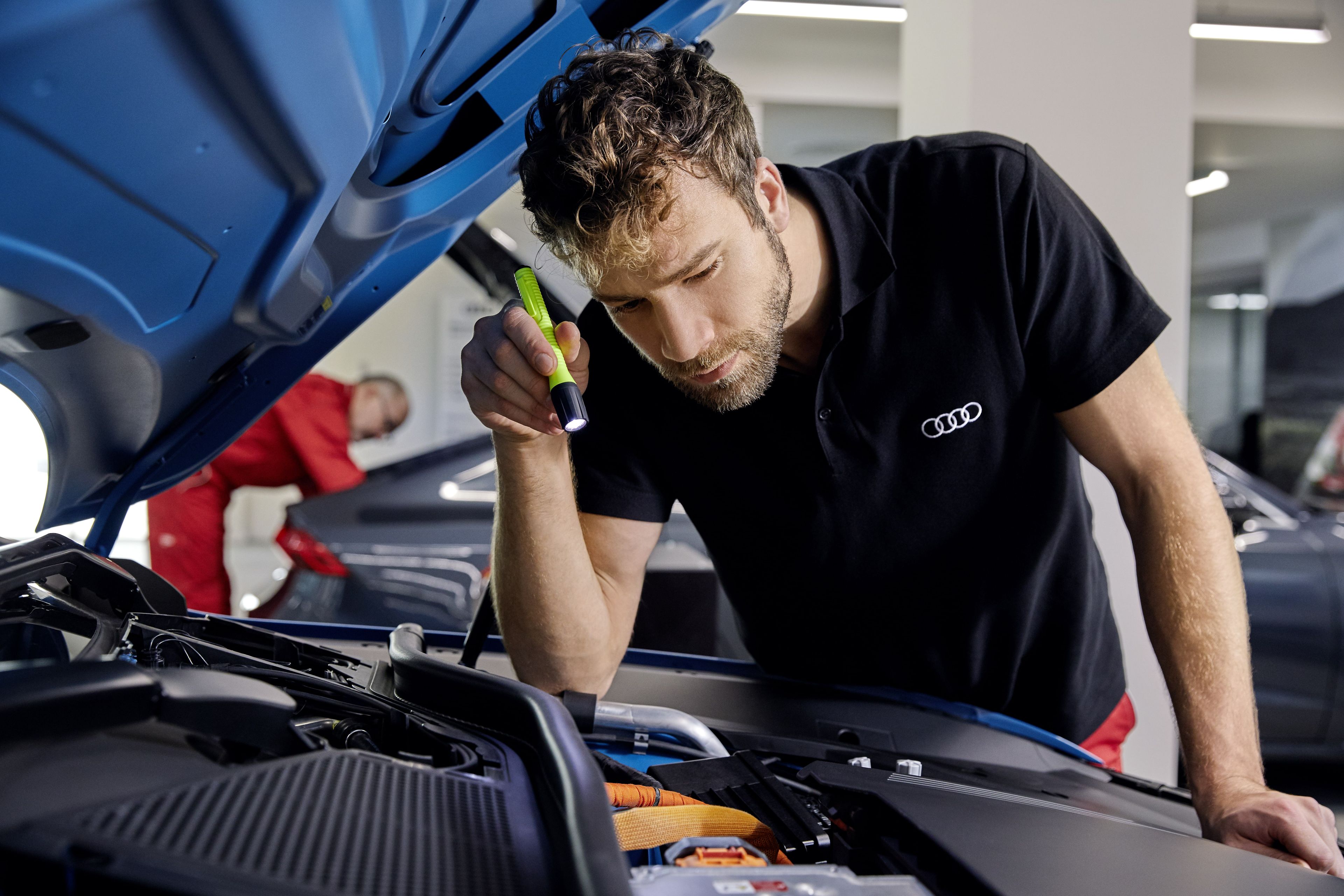 Ein Mechaniker kontrolliert den Motorinnenraum eines Audi Fahrzeugs.