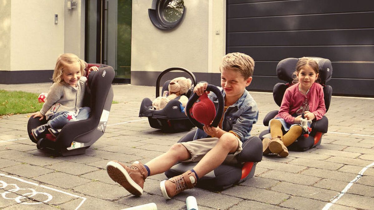 Kinder sitzen in ihren Audi Kindersitzen am Boden 